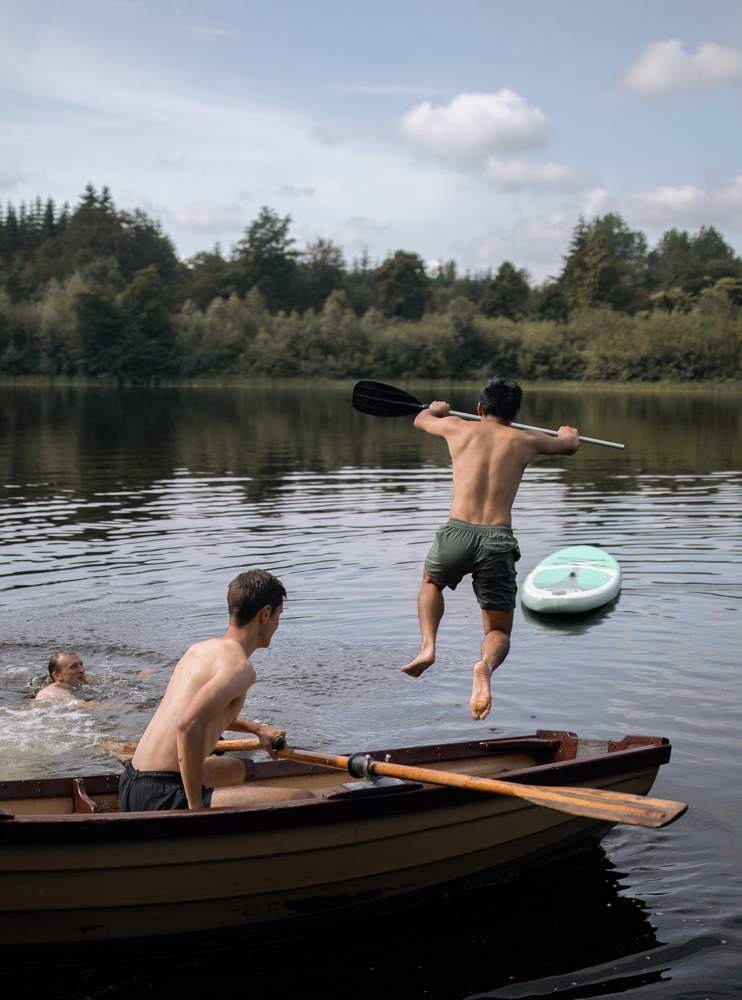 Männer, die vom Ruderboot aus in den See springen und baden.