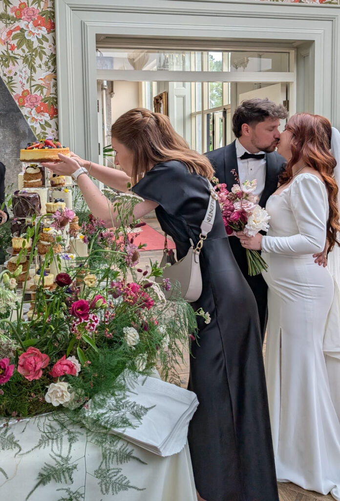 Hochzeitsplaner bereitet den Tortenanschnitt vor und Brautpaar küsst sich im Hintergrund