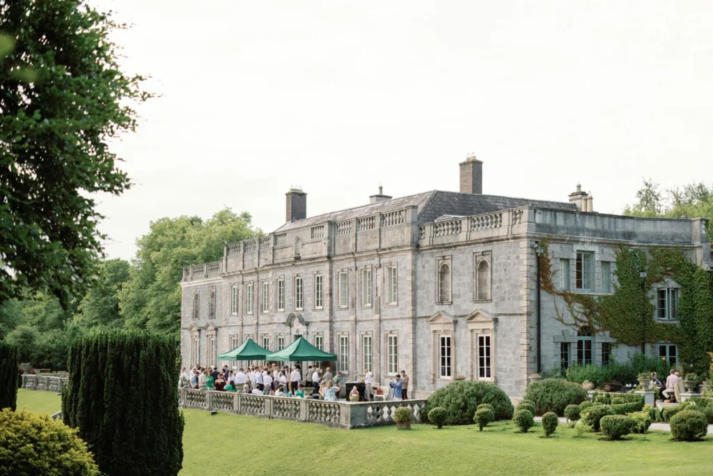 Hochzeitsgesellschaft bei Sonnenuntergang vor der historischen Kulisse des Luxus-Anwesens Gloster House in Irland