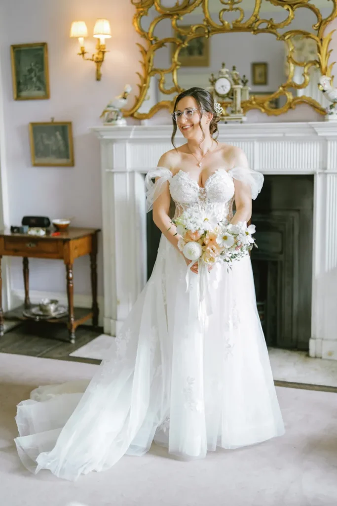 Bridal portrait of a smiling bride holding her bouquet in front of a historic stone fireplace