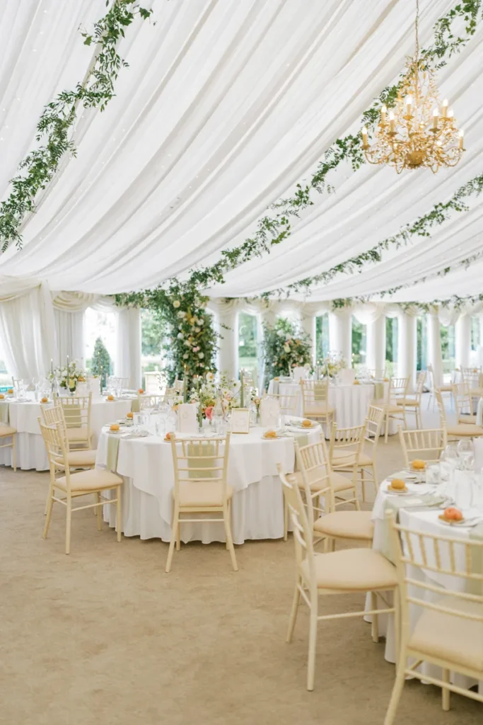 Wide angle shot of Castle Leslie Pavilion featuring ceiling installations, set tables, and a broken floral arch behind the top table