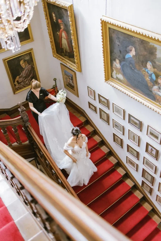 Hochzeitsplanerin Lena Freitag hält die Schleppe und den Brautstrauß, während die Braut die Treppe auf Castle Leslie hinuntergeht
