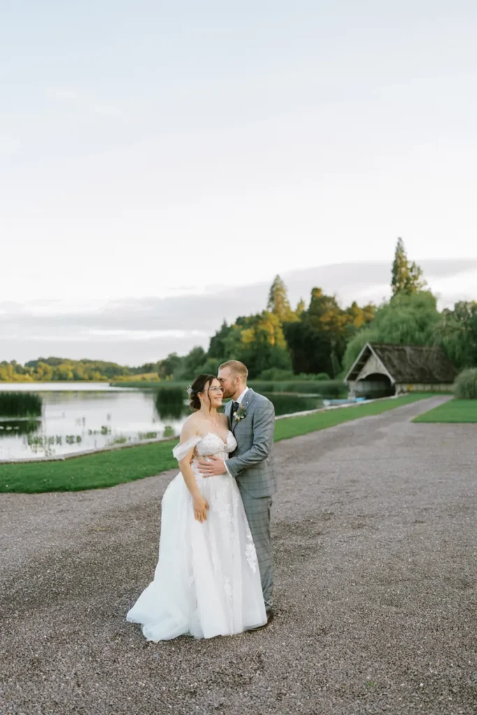 Bräutigam küsst die Braut sanft auf die Wange vor dem See von Castle Leslie Estate